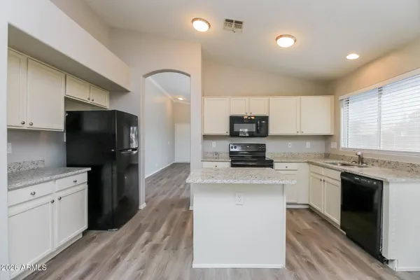a kitchen with stainless steel appliances granite countertop a stove top oven a sink dishwasher a refrigerator and white cabinets with wooden floor