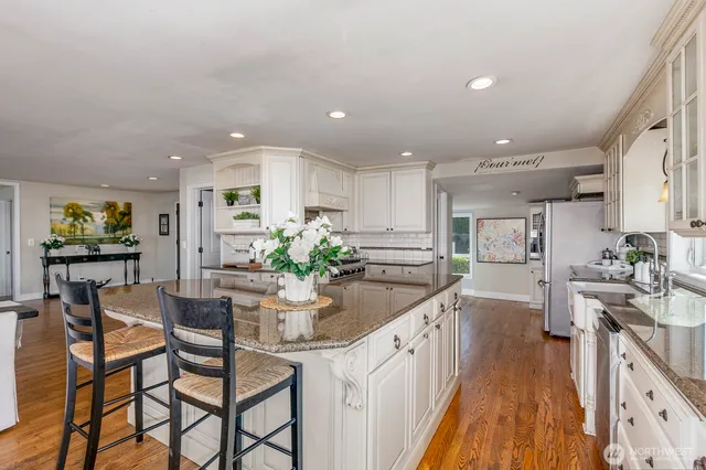 a kitchen with stainless steel appliances kitchen island granite countertop a table chairs in it and a wooden floor