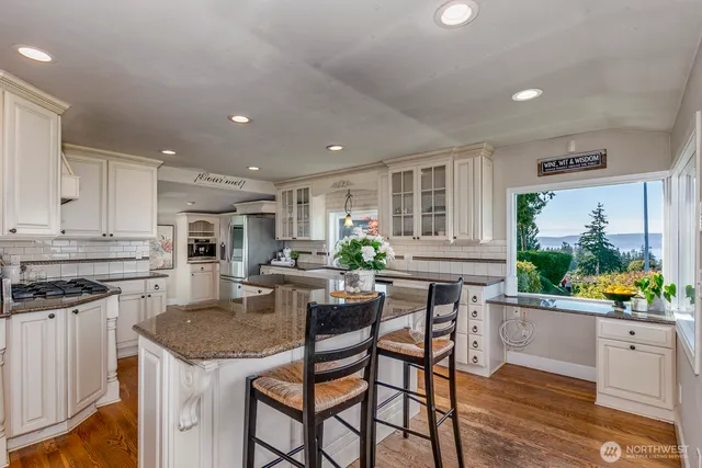 a kitchen with stainless steel appliances granite countertop a stove top oven a sink a dining table and chairs with wooden floor