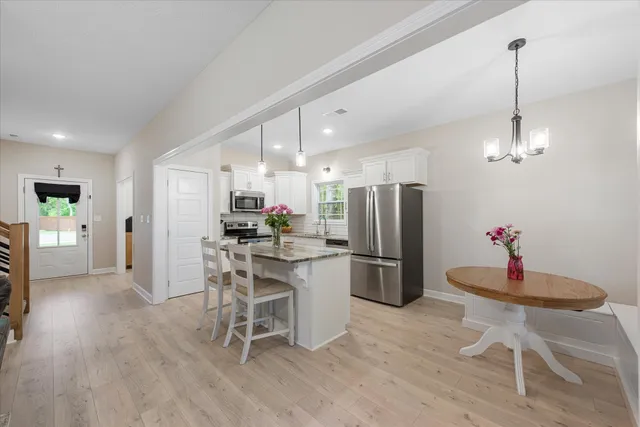 a kitchen with stainless steel appliances kitchen island granite countertop a refrigerator a stove a dining table and chairs with wooden floor