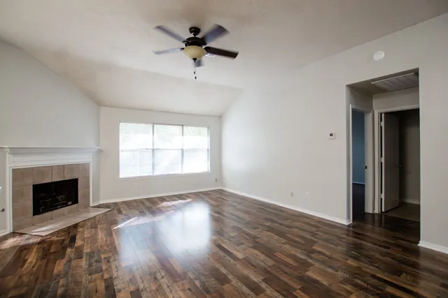 an empty room with wooden floor fan and windows