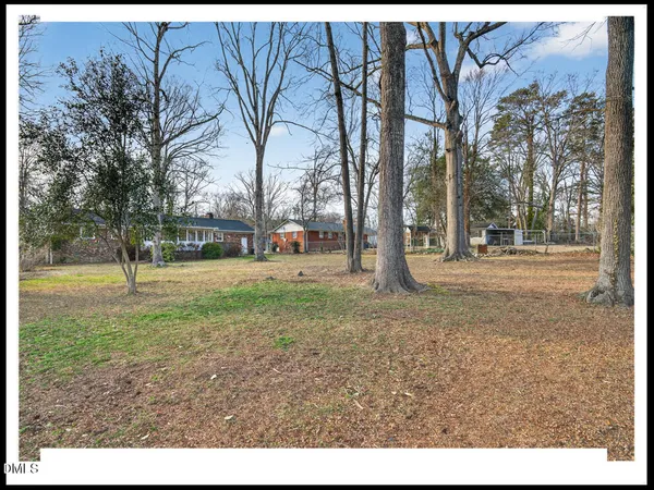 a view of a white house next to a yard with large trees