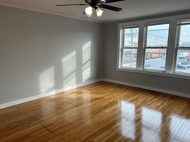 a view of an empty room with wooden floor and a ceiling fan