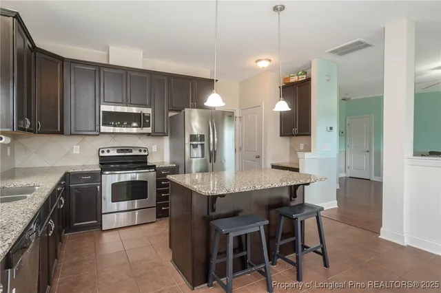 a kitchen with kitchen island granite countertop wooden cabinets a stove a microwave a island with a dining table and chairs