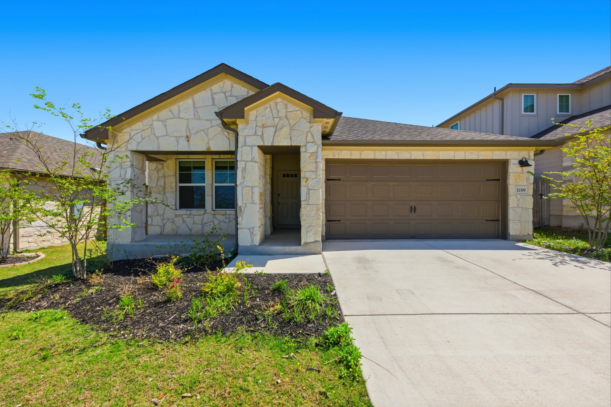 View of front of property featuring stone siding, a garage, and driveway