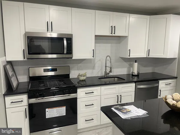 a kitchen with granite countertop a stove a sink and a white cabinets