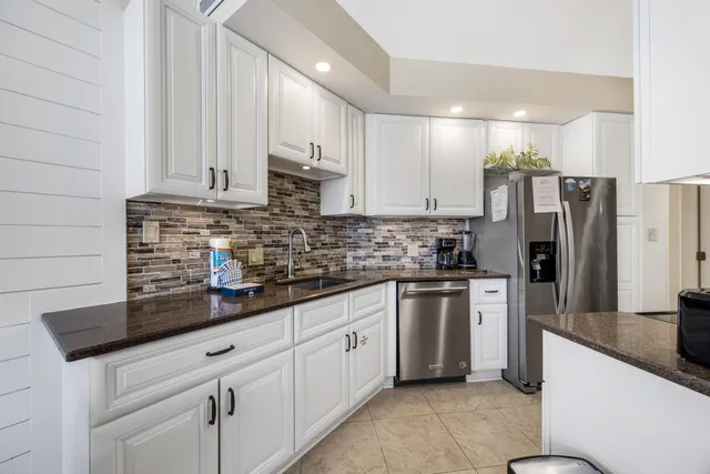 a kitchen with stainless steel appliances granite countertop a sink a stove a refrigerator a white counter space and cabinets