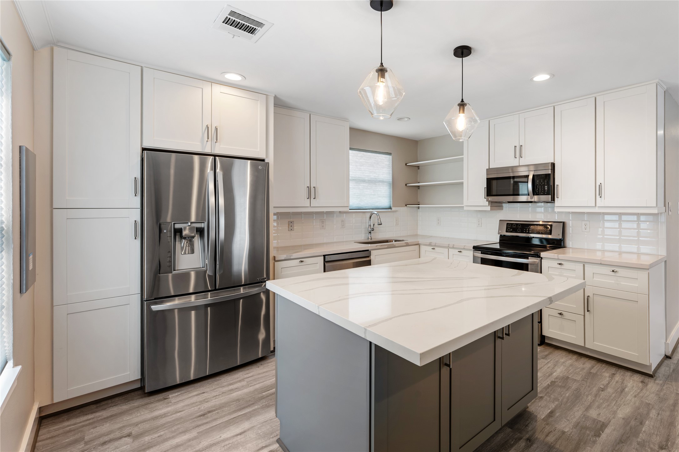 809 East 40th Street Houston, TX 77022 - Photo 6 of 27 Fully updated interior with new flooring, fresh neutral paint, and sleek stainless appliances creates a bright, modern kitchen space. The oversized Quartz island, updated lighting, and built-in pantry with pull-out shelves adds smart, convenient storage.