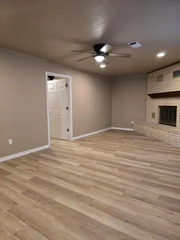 a view of an empty room with wooden floor and a ceiling fan