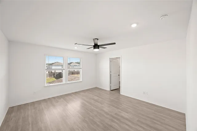 an empty room with wooden floor ceiling fan and windows