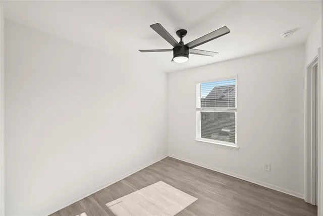 an empty room with wooden floor ceiling fan and windows