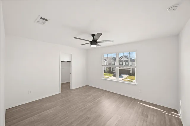 an empty room with wooden floor ceiling fan and windows