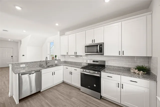 a kitchen with stainless steel appliances granite countertop a stove a sink and white cabinets