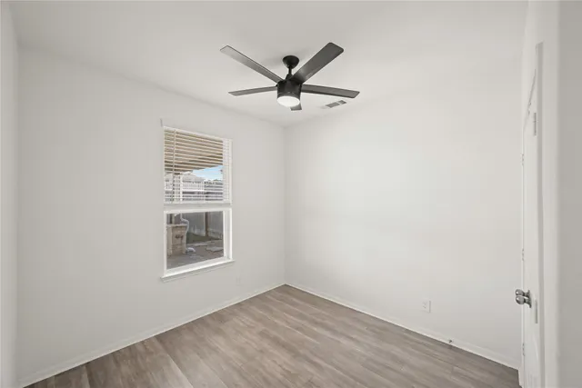 an empty room with wooden floor a ceiling fan and windows