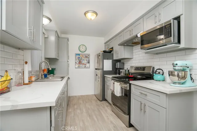 a kitchen with stainless steel appliances a sink a stove top oven a refrigerator cabinets and wooden floor