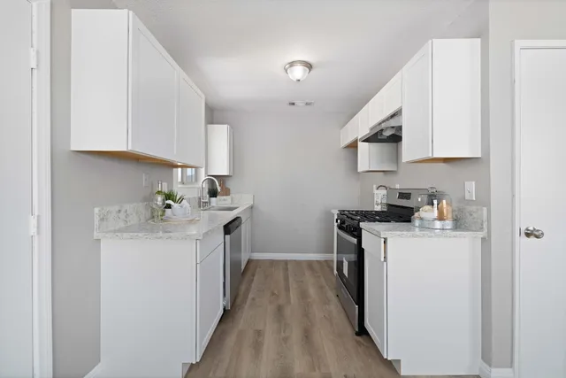 a kitchen with a sink a stove top oven a refrigerator and white cabinets
