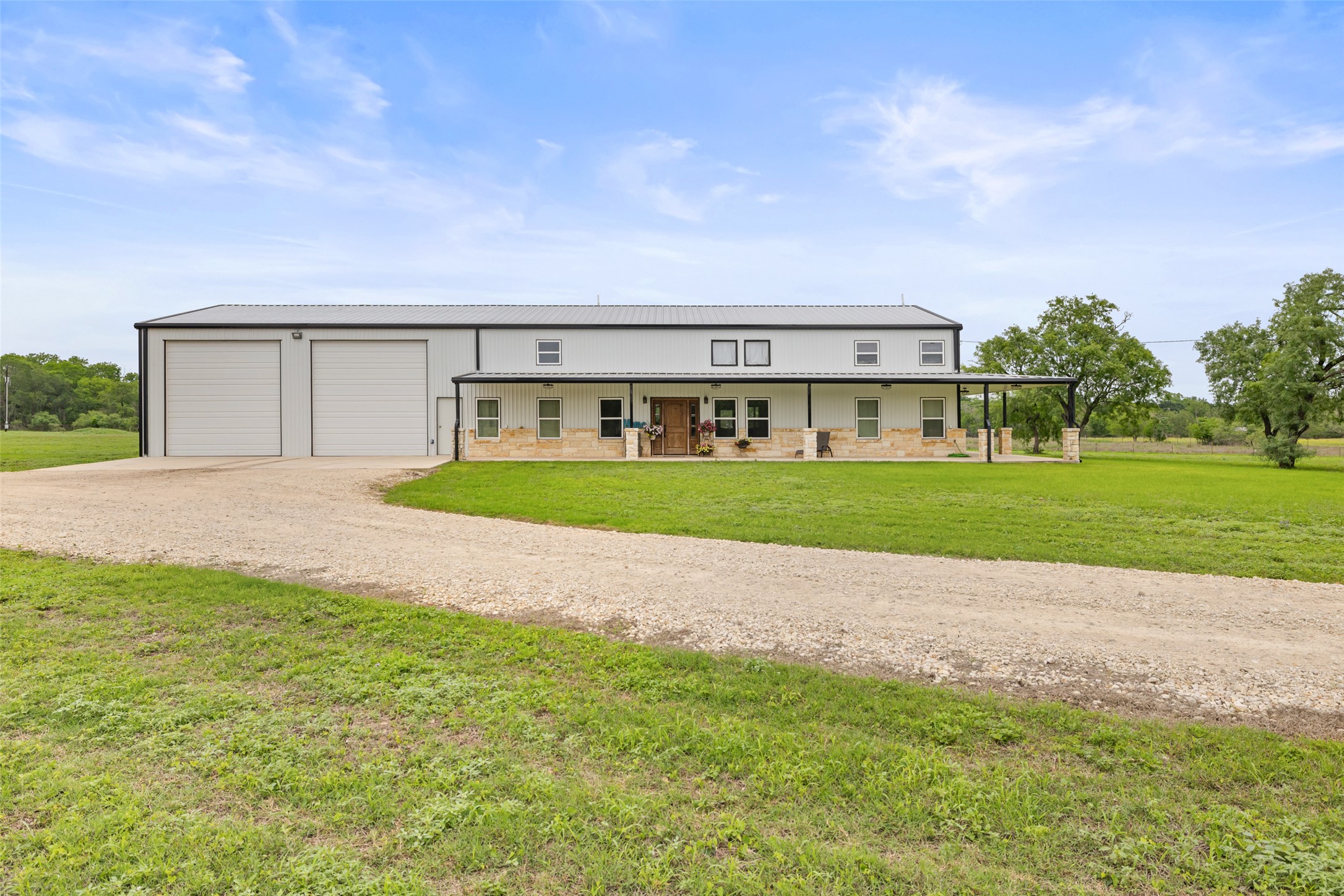 664 Martindale Falls Road Martindale, TX 78655 - Photo 4 of 21 Spacious barn-style residence featuring a gravel driveway, two overhead garage doors, an extended covered front porch with stone accents, and a metal roof
