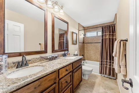 a bathroom with a granite countertop double vanity sink toilet mirror and shower