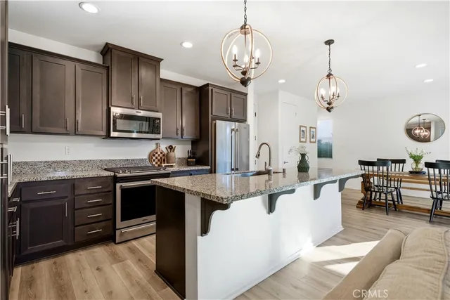 a open kitchen with stainless steel appliances granite countertop a stove refrigerator a sink dishwasher a dining table and chairs with wooden floor