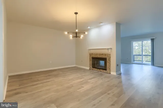an empty room with wooden floor fireplace and chandelier