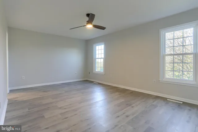 an empty room with wooden floor chandelier and windows