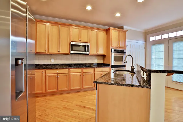 a kitchen with stainless steel appliances granite countertop a refrigerator a stove and a sink with wooden cabinets