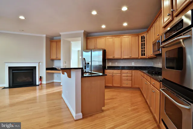 a kitchen with stainless steel appliances granite countertop a refrigerator a stove top oven and a sink with wooden floor