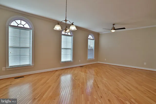 an empty room with wooden floor chandelier fan and windows