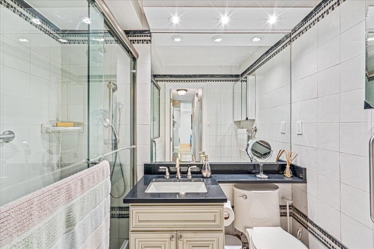 17-85 215th Street, Unit 12S Queens, NY 11360 - Photo 15 of 37 Full bathroom with tile walls, vanity, a stall shower, and decorative backsplash