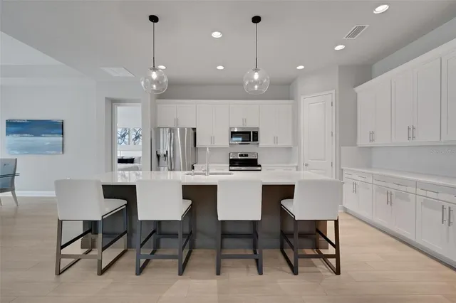 a kitchen with stainless steel appliances kitchen island granite countertop a refrigerator oven a sink a dining table and chairs with wooden floor