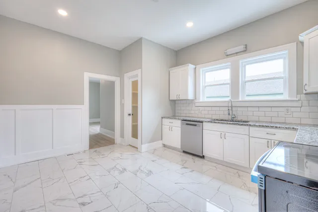 a kitchen with granite countertop a sink white cabinets and a window