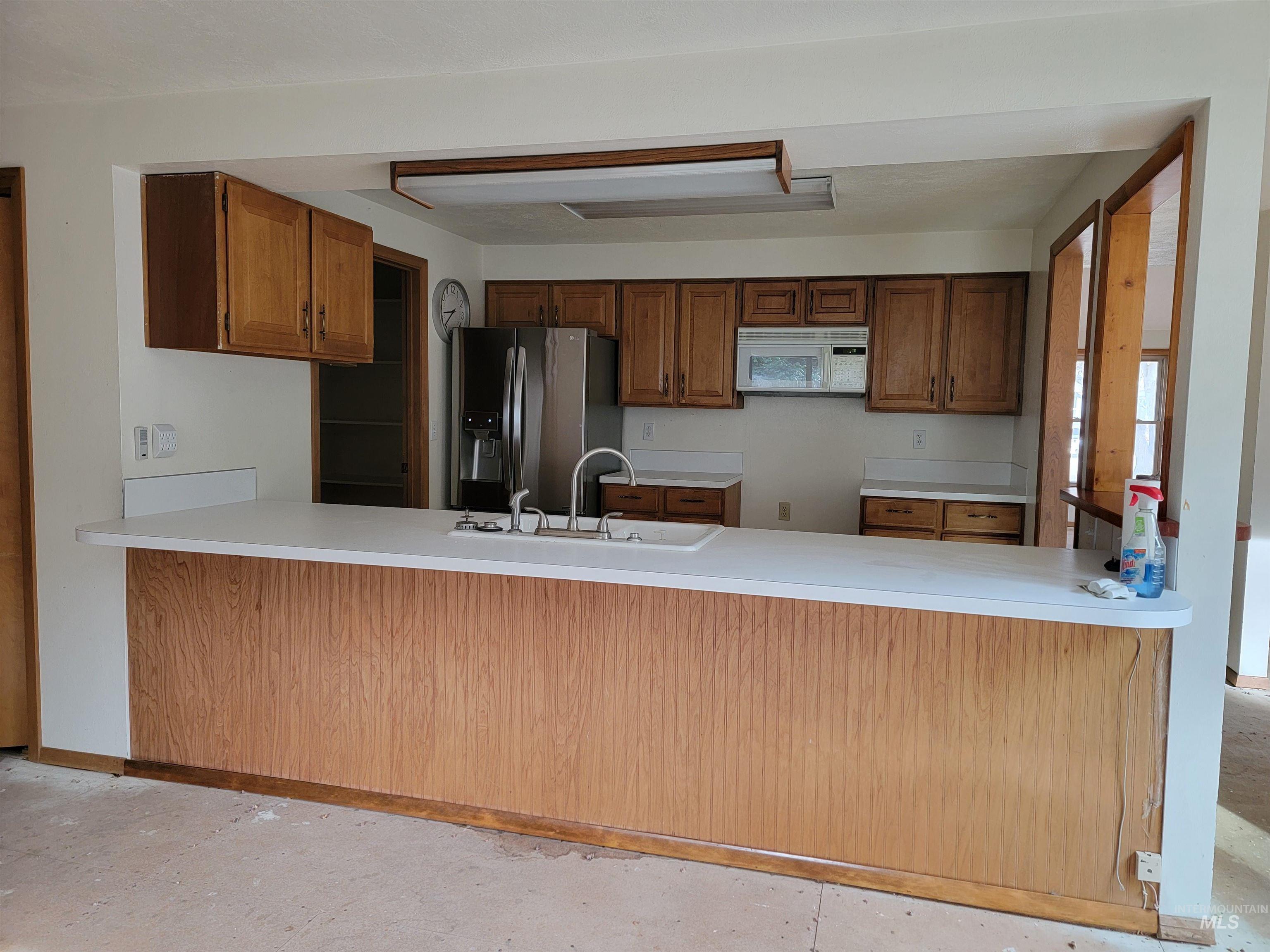3311 Snowflake Way Boise, ID 83706 - Photo 7 of 14 Kitchen featuring brown cabinetry, a peninsula, stainless steel refrigerator with ice dispenser, and white microwave