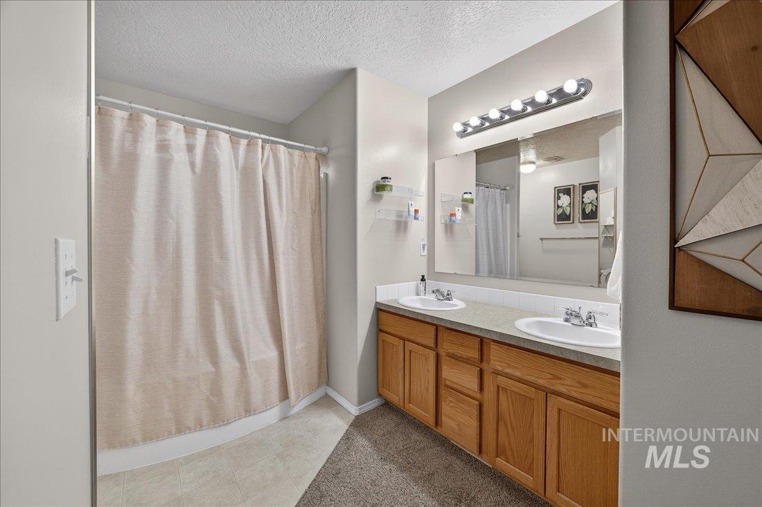 5106 Lathrop Place, Unit 19517 Caldwell, ID 83607 - Photo 29 of 29 Bathroom with double vanity, a textured ceiling, a shower with curtain, and light tile patterned flooring
