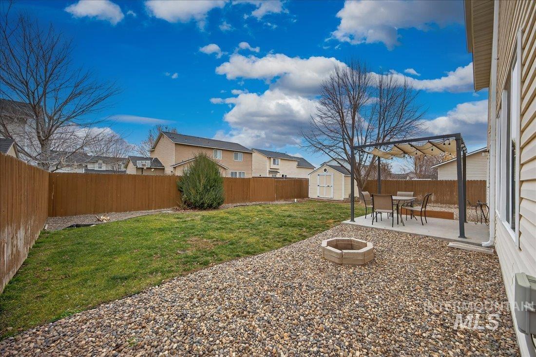 5106 Lathrop Place, Unit 19517 Caldwell, ID 83607 - Photo 7 of 29 Fenced backyard with a storage unit, a patio, a residential view, outdoor dining space, and a fire pit