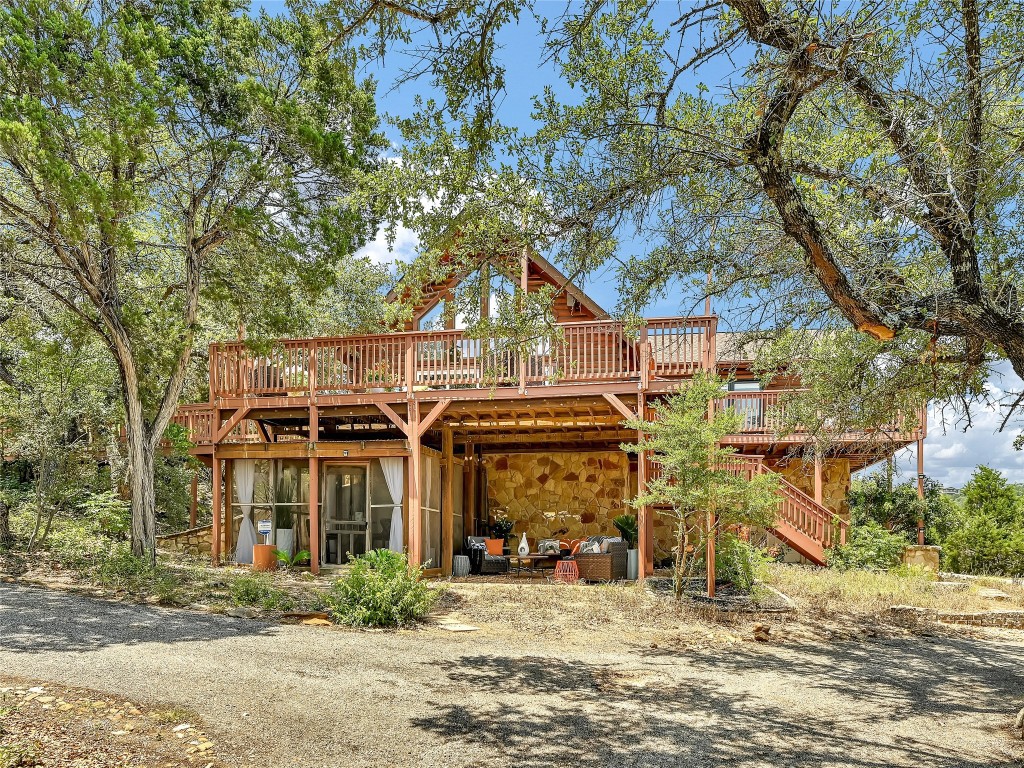 18304 West Reed Park Road Jonestown, TX 78645 - Photo 1 of 24 Mature trees frame a rustic multi-level home with extensive wooden decking and stone details.