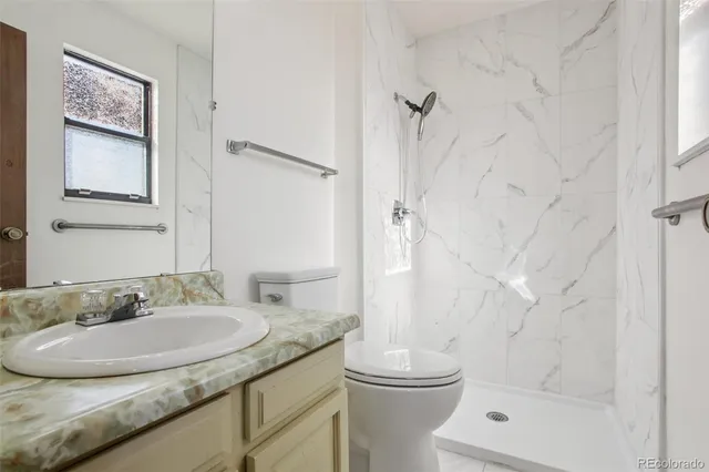 a bathroom with a granite countertop sink a toilet and shower
