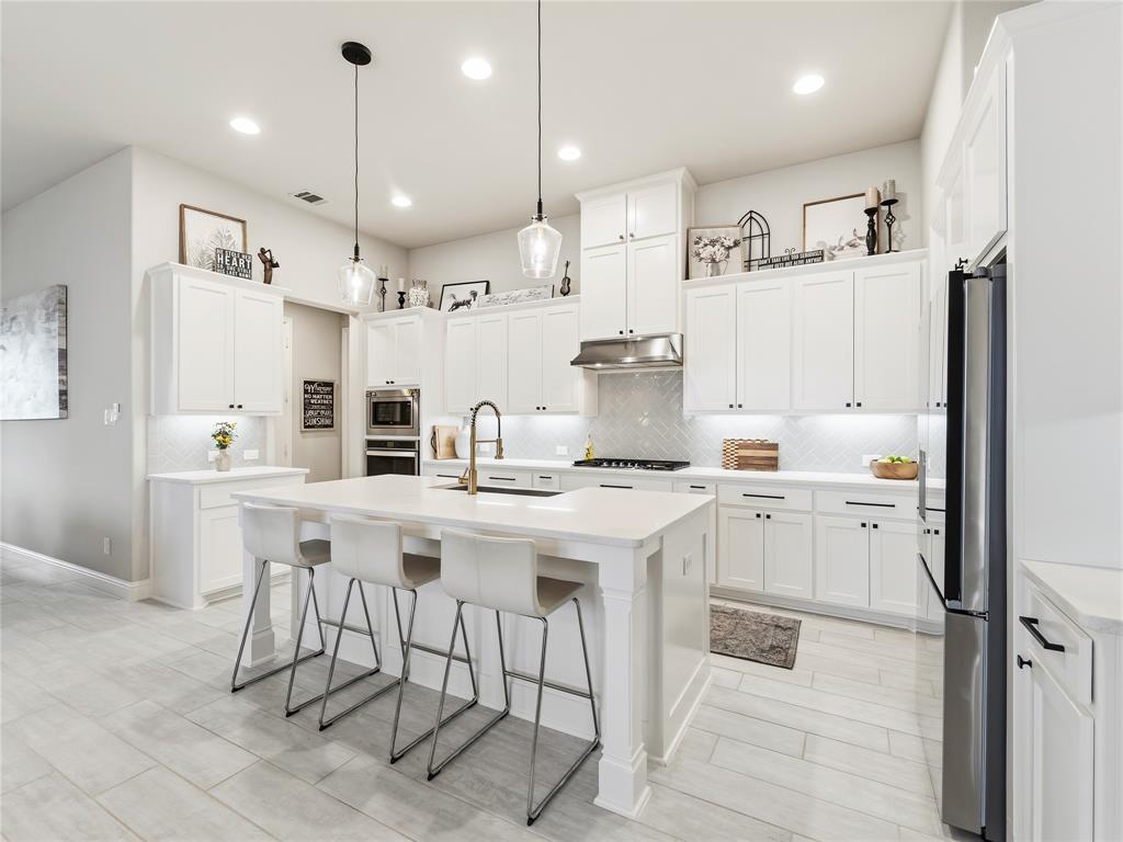 15340 Crape Myrtle Road Frisco, TX 75035 - Photo 10 of 40 Bright kitchen featuring a substantial island with seating, extensive white cabinetry, stainless steel appliances, a herringbone tile backsplash, and recessed lighting