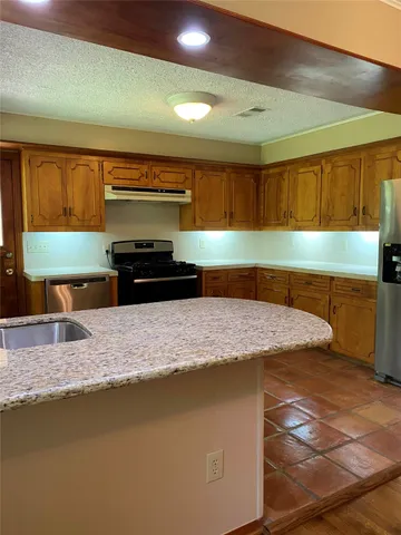 a kitchen with granite countertop a sink a stove top oven a counter space and cabinets