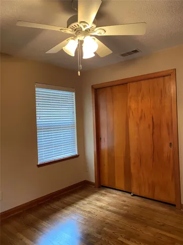 an empty room with wooden floor fan and windows