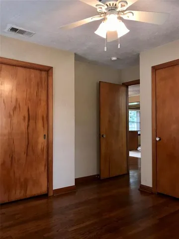 a view of an empty room with wooden floor and a ceiling fan