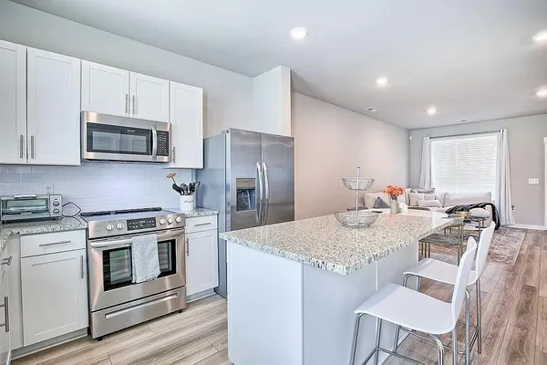 a kitchen with stainless steel appliances granite countertop a stove a sink a refrigerator a dining table and chairs