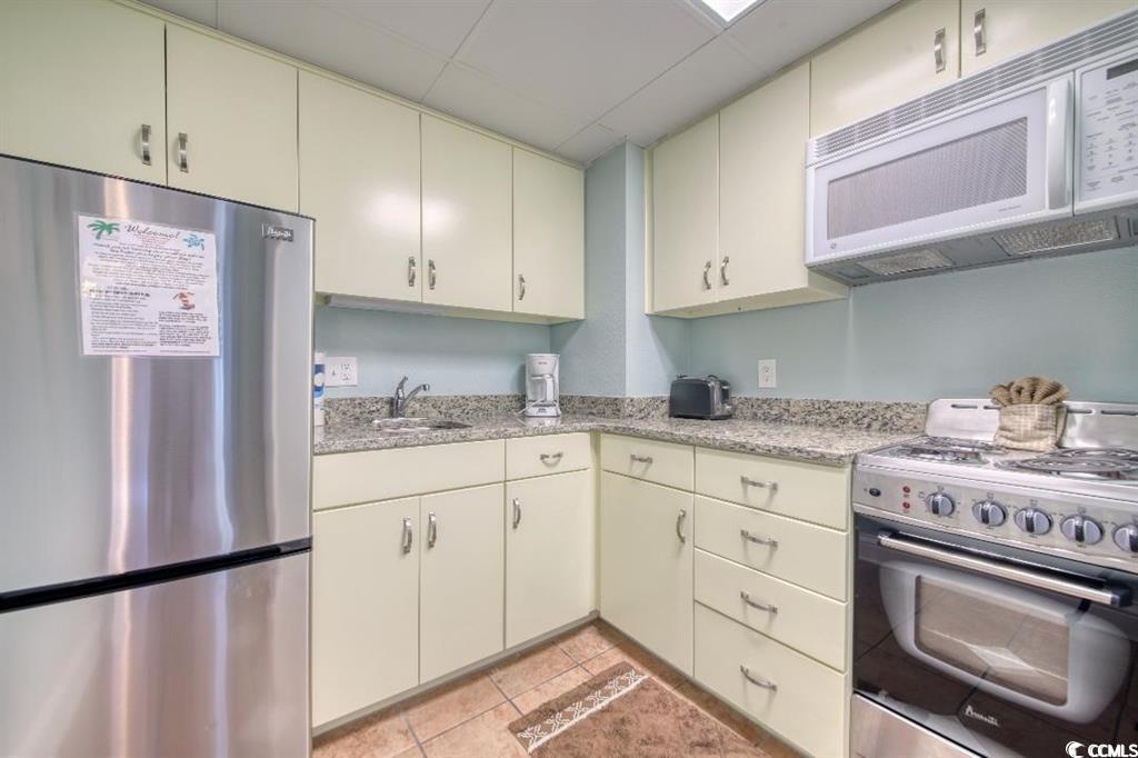 6900 North Ocean Boulevard, Unit 611 Myrtle Beach, SC 29572 - Photo 7 of 17 Kitchen featuring cream cabinetry, freestanding refrigerator, range with gas stovetop, white microwave, and a drop ceiling