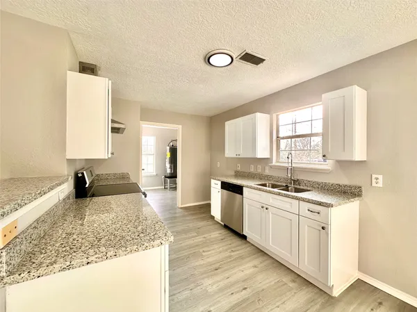 a large kitchen with granite countertop a sink and white cabinets with wooden floor