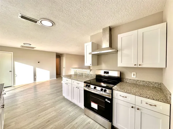 a kitchen with granite countertop a stove a sink and white cabinets with wooden floor