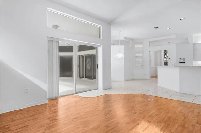 a view of an empty room with wooden floor and a kitchen