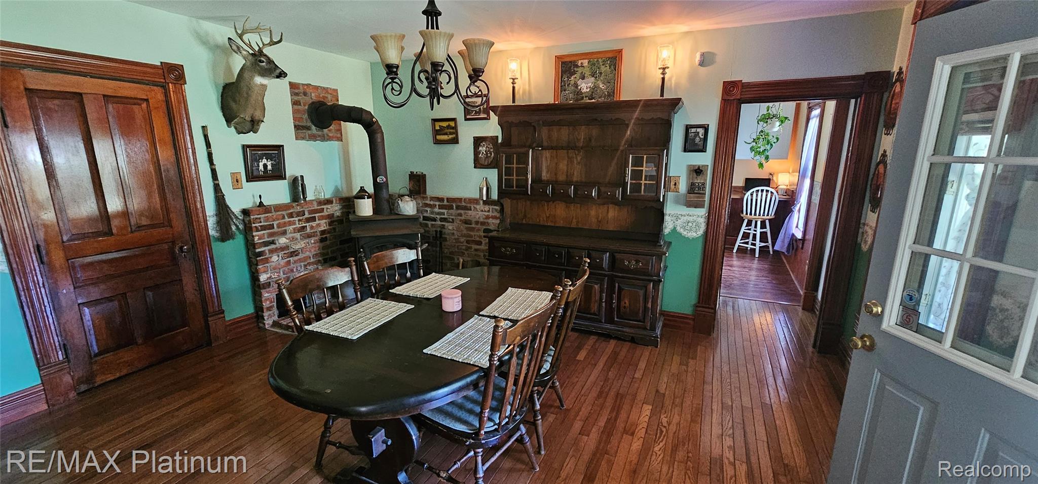 17140 Haggerty Road Belleville, MI 48111 - Photo 12 of 42 Hardwood flooring throughout featuring a brick accent wall with an installed stove, an ornate chandelier, and wood-paneled doors with detailed trim