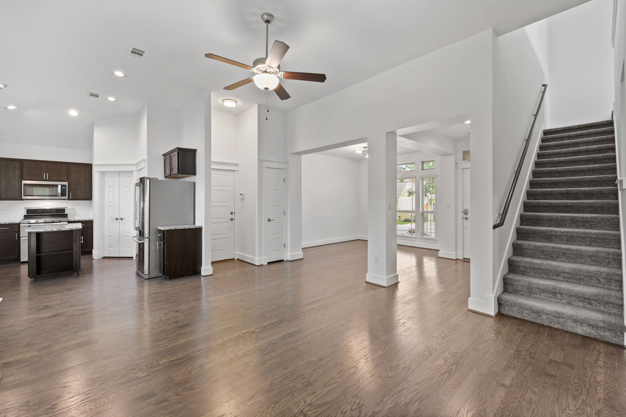 1765 Rowdy Loop, Unit 47 Leander, TX 78641 - Photo 15 of 39 Hardwood-finish flooring throughout the main living areas, featuring a kitchen with dark wood cabinetry and a white subway tile backsplash, recessed lighting, a modern ceiling fan, and a carpeted staircase with a dark handrail
