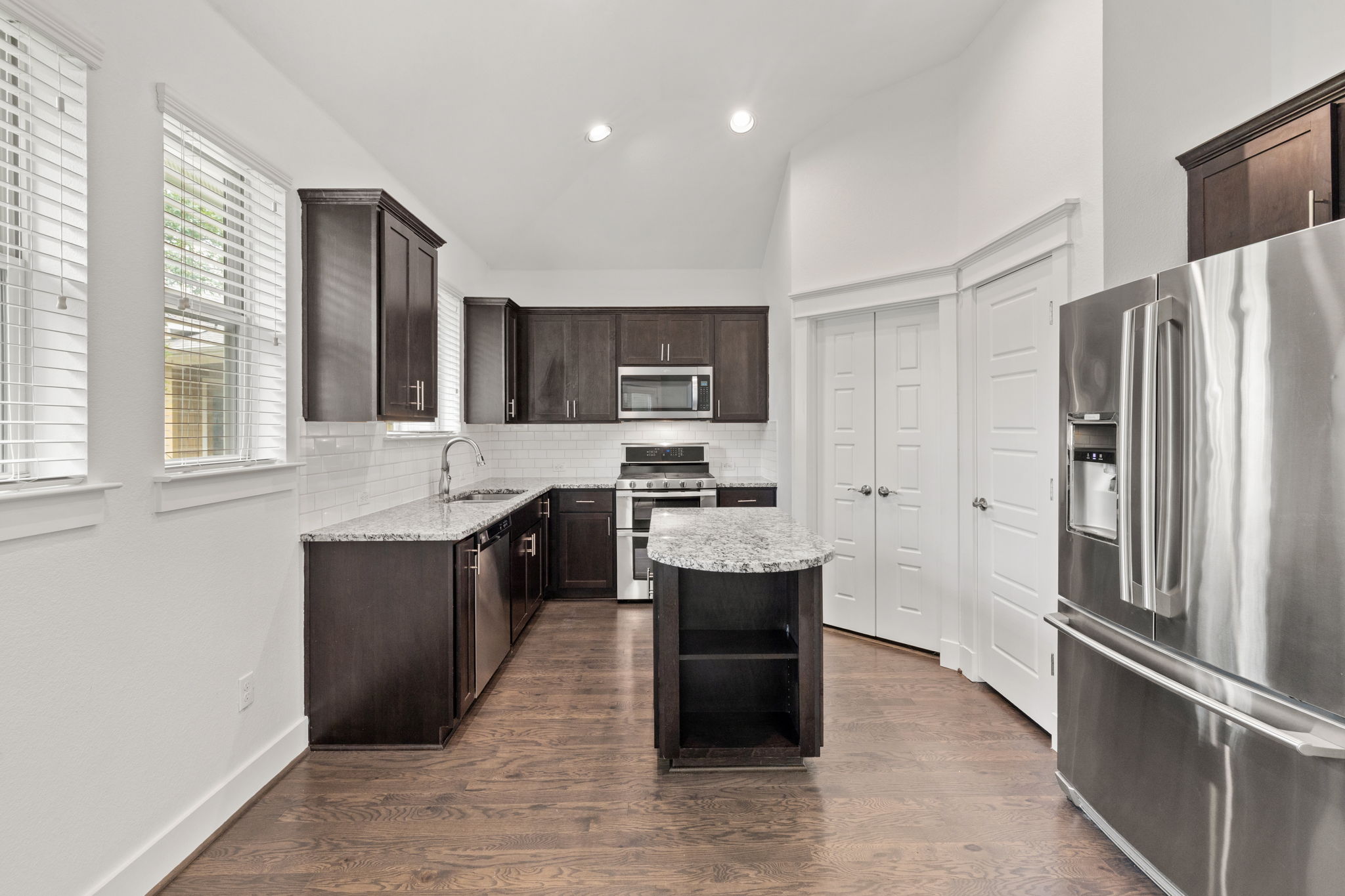 1765 Rowdy Loop, Unit 47 Leander, TX 78641 - Photo 16 of 39 Kitchen featuring dark wood cabinetry, stainless steel appliances, granite countertops, a subway tile backsplash, and wood-finish flooring