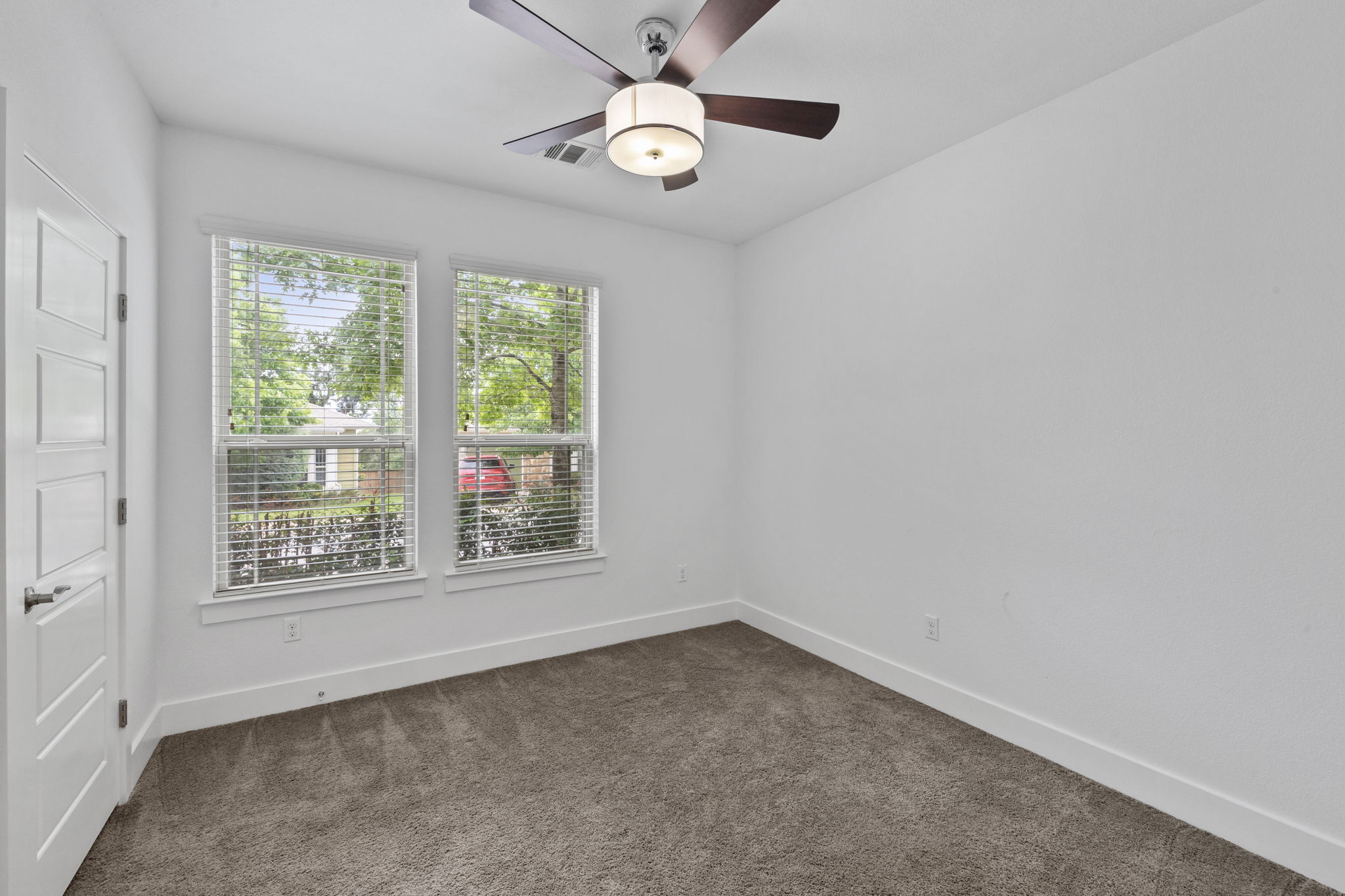 1765 Rowdy Loop, Unit 47 Leander, TX 78641 - Photo 21 of 39 Carpeted room featuring two windows with blinds, a modern ceiling fan with integrated lighting, and a contemporary five-panel door with a dark handle
