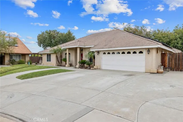 a view of a white house in front of a big yard with plants and large trees